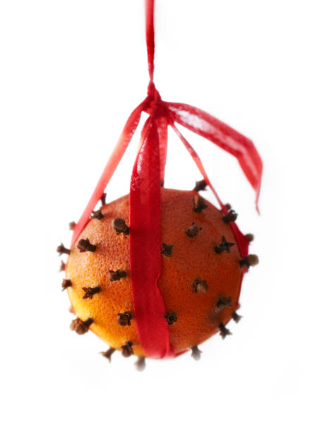 Clove-studded orange tied with red ribbon suspended against white background, evoking festive and aromatic ambiance.