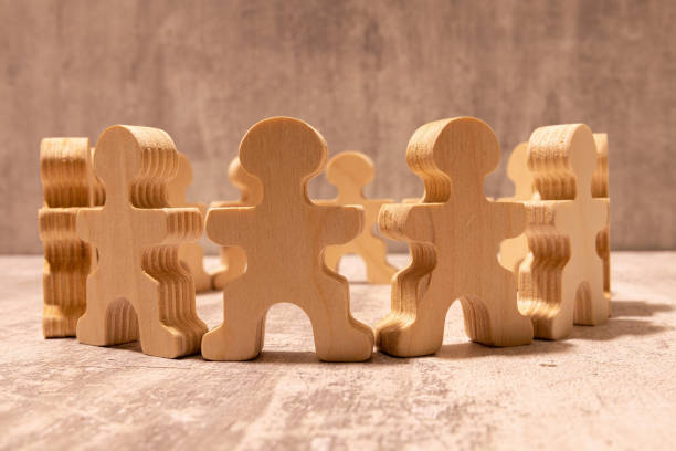 istock Many different paper human figures standing in circle on wooden table against beige background. 2192442064