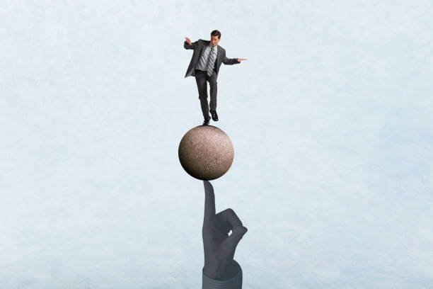 istock Man Balancing On A Sphere That Balances On The Tip Of A Man's Finger 2192442480