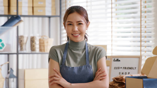 istock Go green use eco friendly packaging box in net zero waste store asian seller retail home office shop. Small SME owner young adult asia Gen Z people happy relax smile pride arm cross looking at camera. 2192443534