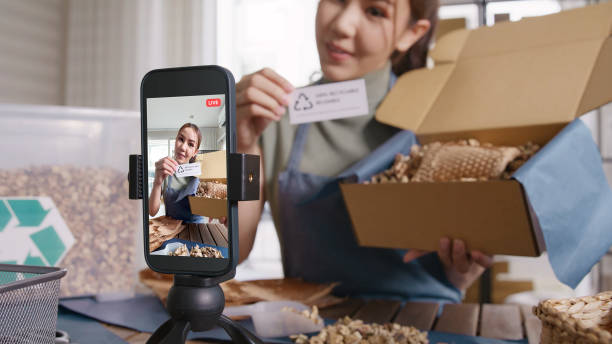 istock SME owner go green net zero retail store live stream talk on phone showing eco care plastic free packaging box. Asia people young woman record video on tiktok IG reel instagram shop happy side hustle. 2192443584