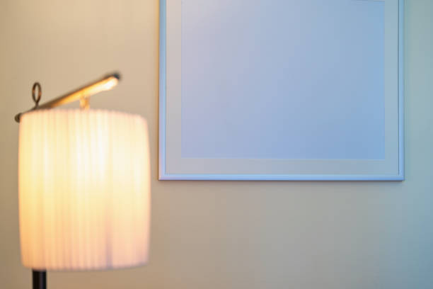 A classic table lamp casts a warm glow near a framed blank canvas on a pale wall, reflecting the understated sophistication of a vintage boutique hotel interior.