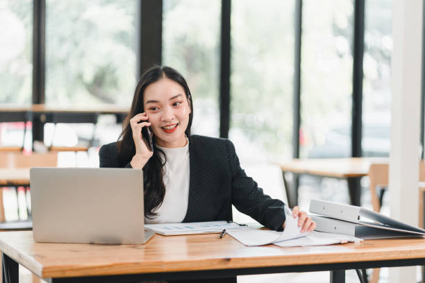 istock professional woman engaged in phone call while working at desk with laptop and documents. She appears focused and productive in modern office setting 2192450201