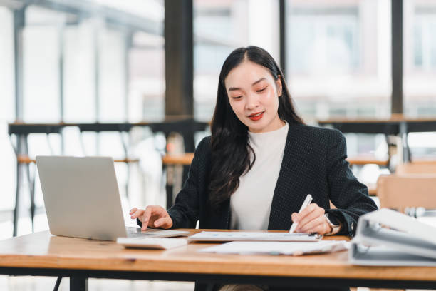 istock professional woman working at desk with laptop, taking notes and focused on her tasks. She is dressed in stylish blazer, showcasing modern office setting 2192450208