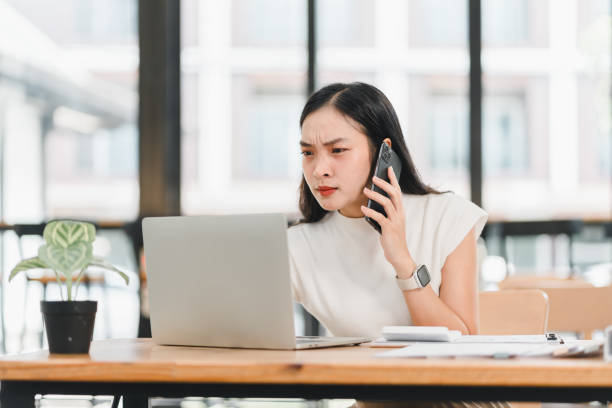 istock Focused woman working on laptop while talking on phone, showing determination and concentration in modern office space 2192451773