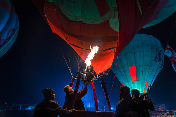 A glowing hot air balloon drifts through the deep blue twilight sky in Cappadocia, Urgup, Nevsehir, Turkey. The balloon's burner casts a warm golden light, contrasting beautifully against the cool tones of the evening. Cappadocia’s famous balloon rides offer breathtaking views at dawn and dusk, creating unforgettable moments for travelers