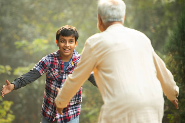 Rear view of playful grandfather running towards cheerful grandson for embracing while spending leisure time in garden