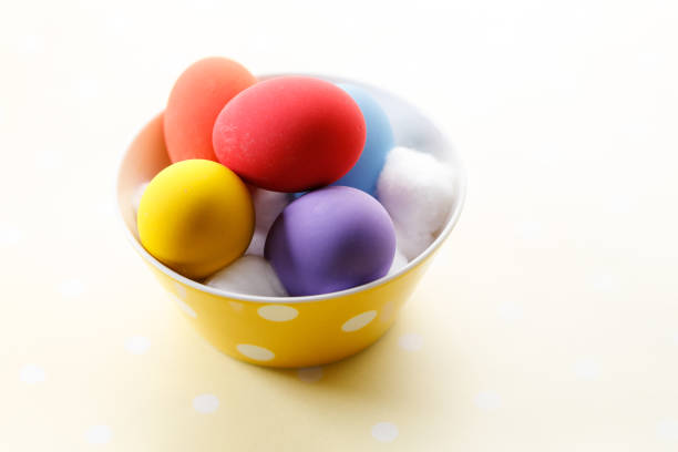 Happy Easter eggs in a bowl on dot yellow color background. Easter decoration Selective focus.
