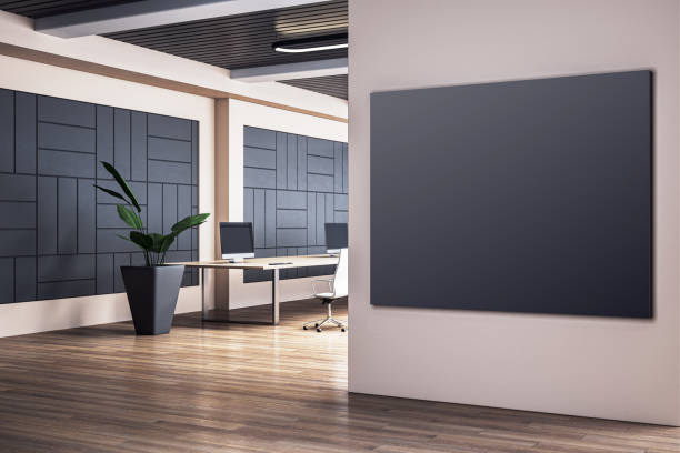 Modern office interior with blank black frame on wall, wooden flooring, computer desks, and plant in a pot, creating a professional atmosphere. 3D Rendering