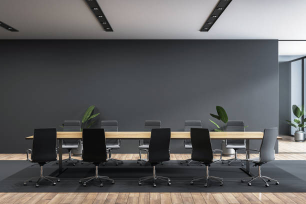 Modern boardroom interior with long table, black chairs, plants, and wooden flooring in a bright, contemporary office space. 3D Rendering