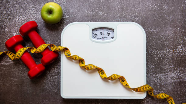 istock Weight loss control planning.  White scale and measuring tape with green apple, dumbbell for body dieting healthy life. Top view 2192470831