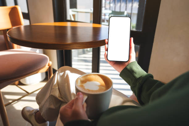 istock Mockup image of a woman holding mobile phone with blank desktop screen while drinking coffee in cafe 2192472496