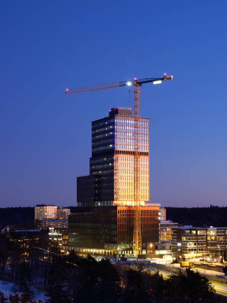 Modern glass facade skyscraper building with a crane against clear sky background, constructing Sickla Central office building