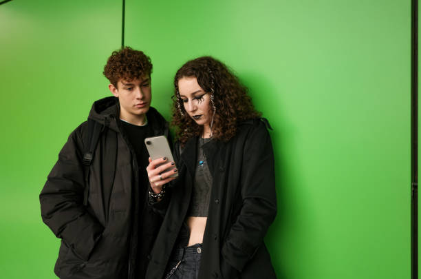 istock Curly-haired duo standing in front of green wall and using phone 2192494147