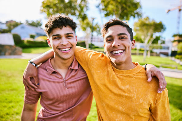Portrait of two male friends, one with arm around the other, smiling toward camera stock photo