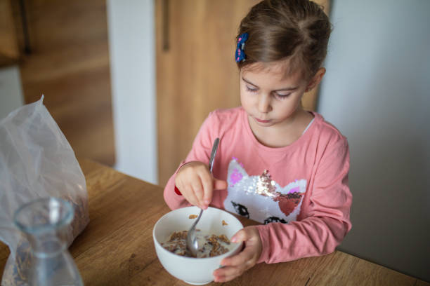 Cute little girl eating corn flakes in kitchen