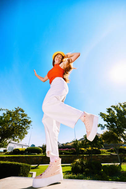 Young woman standing on one leg against clear blue sky, low angle