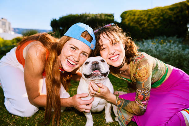 Two young women smiling towards camera, stroking pet dog