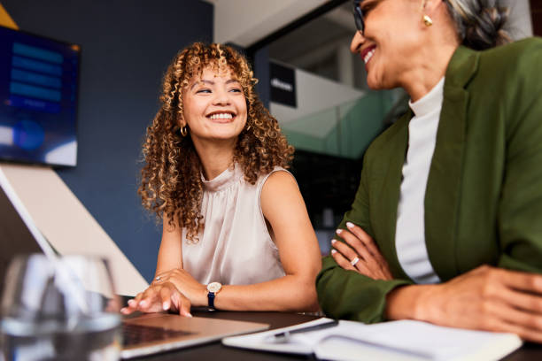 Cheerful young businesswoman smiling confidently towards female colleague at work stock photo