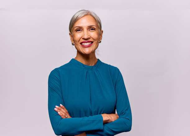 Studio portrait of cheerful mature woman with gray hair wearing blue blouse, arms folded stock photo