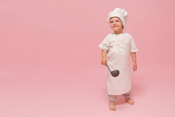 istock A cute boy in a chef's uniform is holding a culinary instrument ladle. Studio portrait on a pink background. Kid aged 3 years (three year old boy) 2192499296