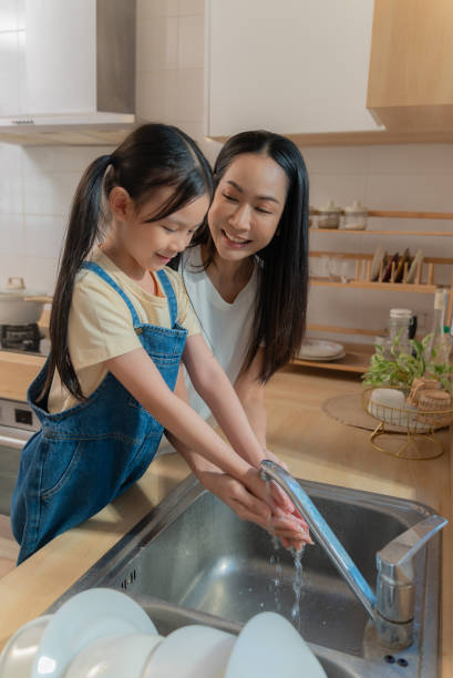 istock Asian Mother Teaching Her Daughter Proper Handwashing at Kitchen Sink 2192504128