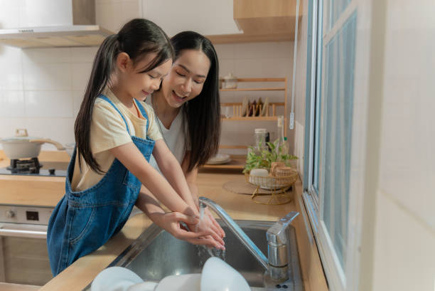 istock Asian Mother Teaching Her Daughter Proper Handwashing at Kitchen Sink 2192504148