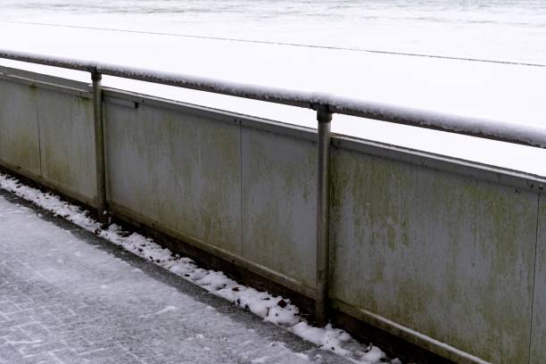Fresh snow covers a metal railing and paved walkway next to a field, creating a serene winter scene
