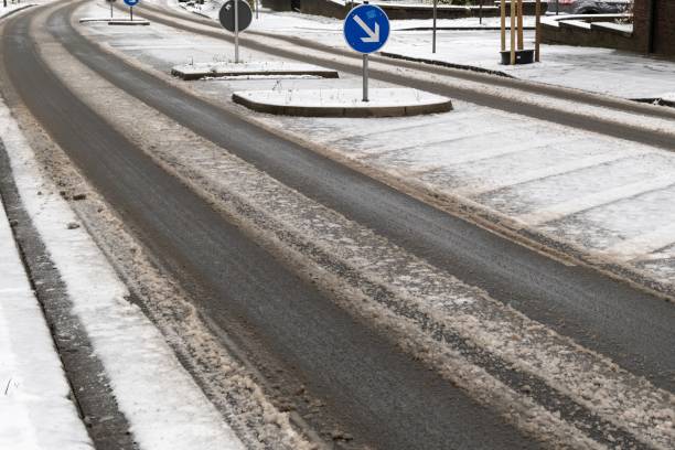 Melting snow creates tracks on a partially cleared asphalt road during the winter season, with a keep left sign indicating traffic flow