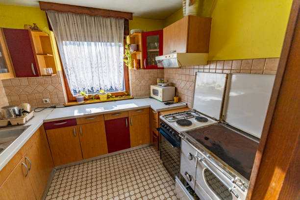 Cozy kitchen featuring wooden cabinets, retro appliances, and a patterned tile floor. Natural light filters through the lace-curtained window, highlighting the warm yellow walls and charming decor. A functional and nostalgic cooking space evokes a sense of timeless comfort.