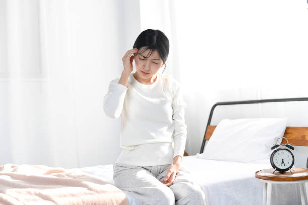 頭痛に苦しむベッドに座っている若いアジア人女性 - うつ病 ストックフォトと画像