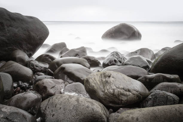 Long exposure photography of rocks emerging from the misty sea in Vila Nova de Gaia, Portugal, creating a mysterious and evocative atmosphere