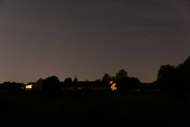 istock A quiet rural scene at night with softly illuminated farmhouses surrounded by trees under a starry sky. 2192518037