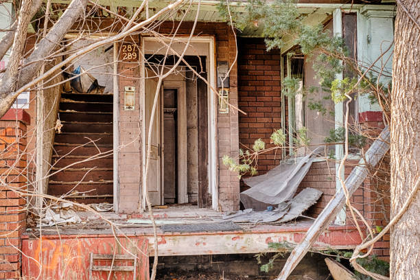 The porch of an abandoned duplex is torn apart with open doors and junk strewn all over.