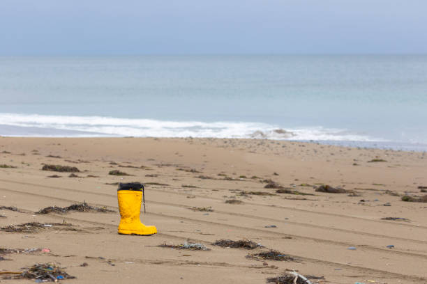 Yellow rubber boot stands on the sandy ocean shore. Beach pollution