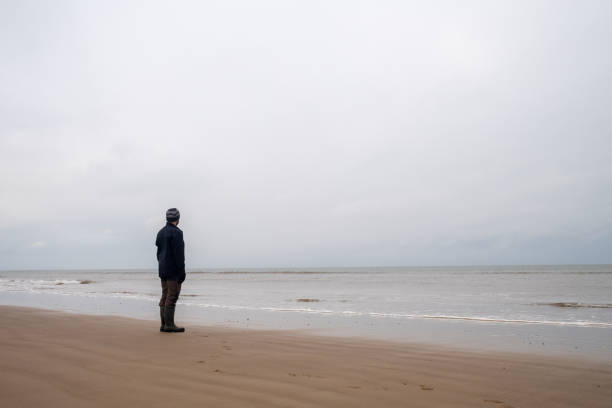 istock Man standing on a beach looking out to sea 2192523131