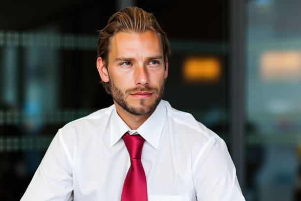 Thoughtful businessman wearing a white shirt and red tie, gazing away in a modern office, reflecting on aspirations and strategies for success in a corporate environment