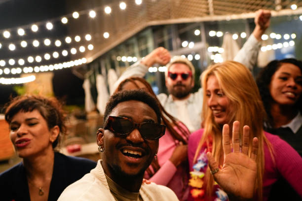 Young multiethnic friends enjoying rooftop party, waving and dancing