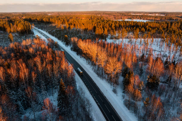 istock Straight Road Through Snow Covered Forest at Sunset with Vehicle 2192535622