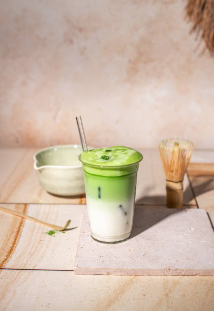 Green Tea Iced Matcha Latte prepared fresh on bright kitchen counter with milk, ice cubes and frothy matcha foam