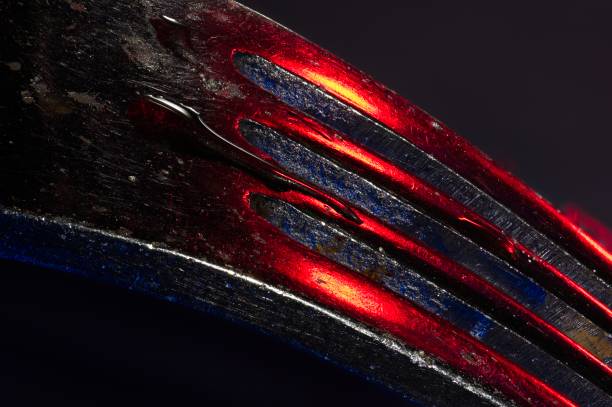 Abstract of tines of a chrome fork with red and blue reflections and a drop of water