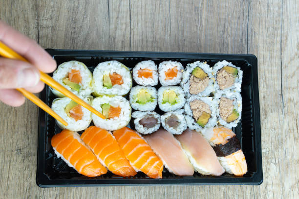 istock From above anonymous hand with chopsticks eating assorted sushi rolls served on tray on wooden restaurant table with copy space. 2192542207