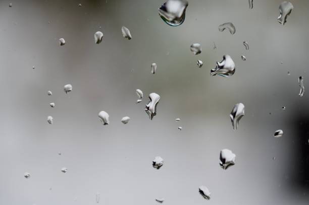 Water droplets on a glass surface with a cloudy gray sky in the background. A simple yet emotional representation of rainy weather and calm introspection.