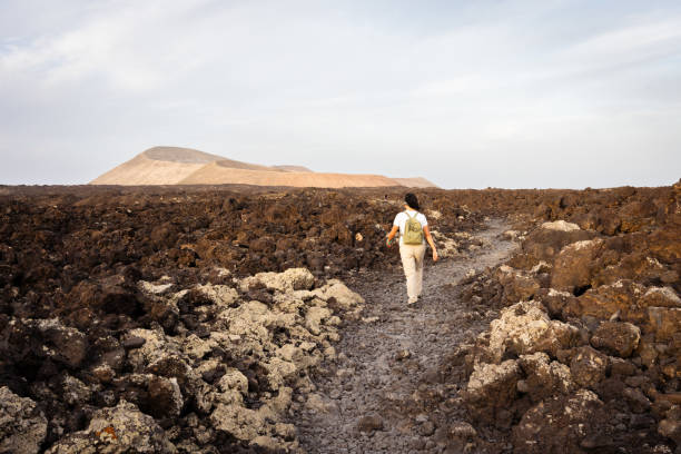 istock Female hiker trekking volcanic terrain, back turned, navigating solidified lava flow through dramatic Timanfaya National Park landscape in Lanzarote, Canary Islands 2192545395