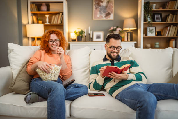cheerful couple enjoy together on sofa with book and popcorn