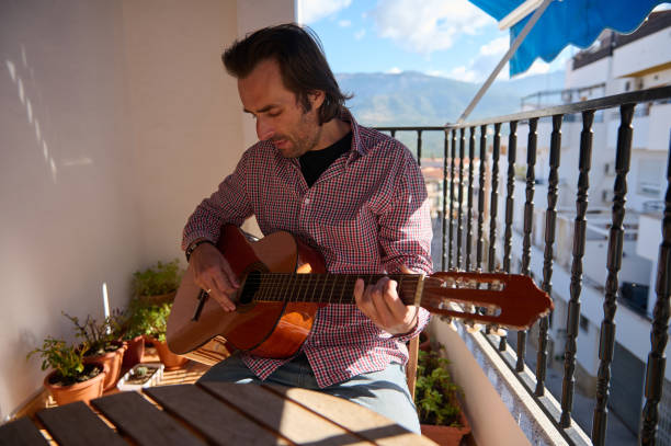 istock Man playing guitar on a sunny balcony with mountain views 2192553128
