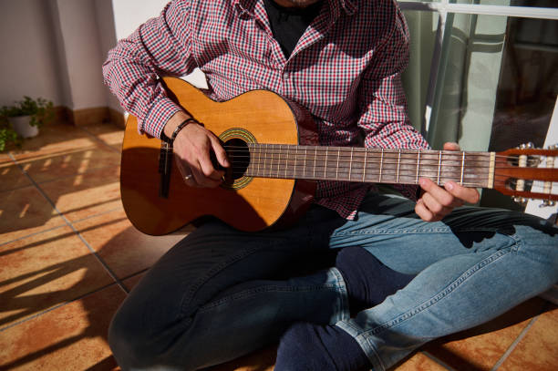 istock Man playing acoustic guitar while sitting on a sunlit tiled floor 2192553129