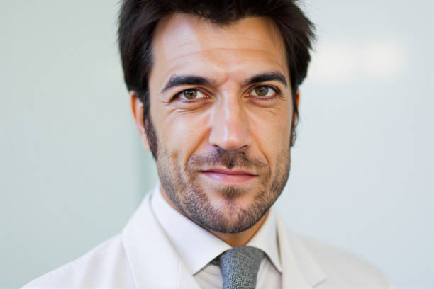 Close-up portrait of a confident male doctor wearing a lab coat and tie, looking directly at the camera with a serious expression, conveying professionalism and expertise in healthcare