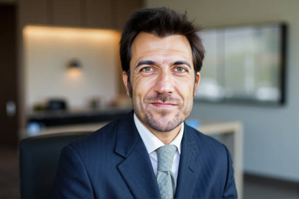 Portrait of a mid adult businessman smiling confidently while sitting in a modern office, wearing a suit and tie, looking directly at the camera