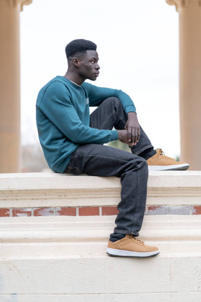 istock Young man sitting on a low wall is looking away and thinking 2192557793